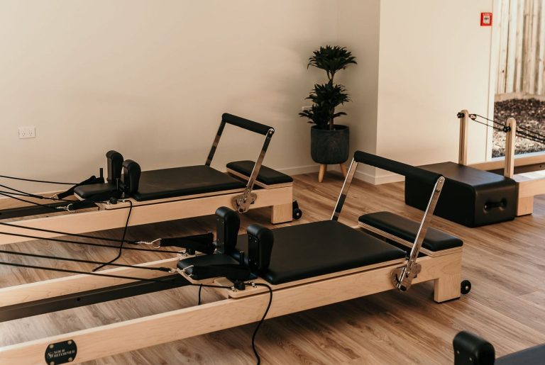 Clinical Pilates studio setup with reformer machines and a screen displaying guided exercises.
